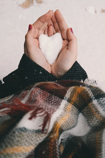 Hands holding heart-shaped snow in winter plaid scarf