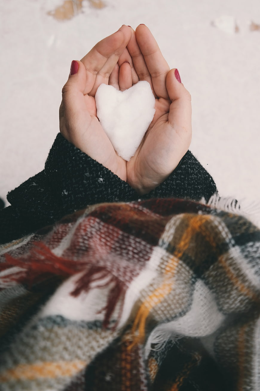 Hands holding heart-shaped snow in winter plaid scarf