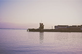 Silhouette of pier and buildings at dusk over calm ocean