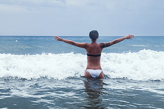 Woman in Bikini Standing in Ocean Waves with Arms Outstretched
