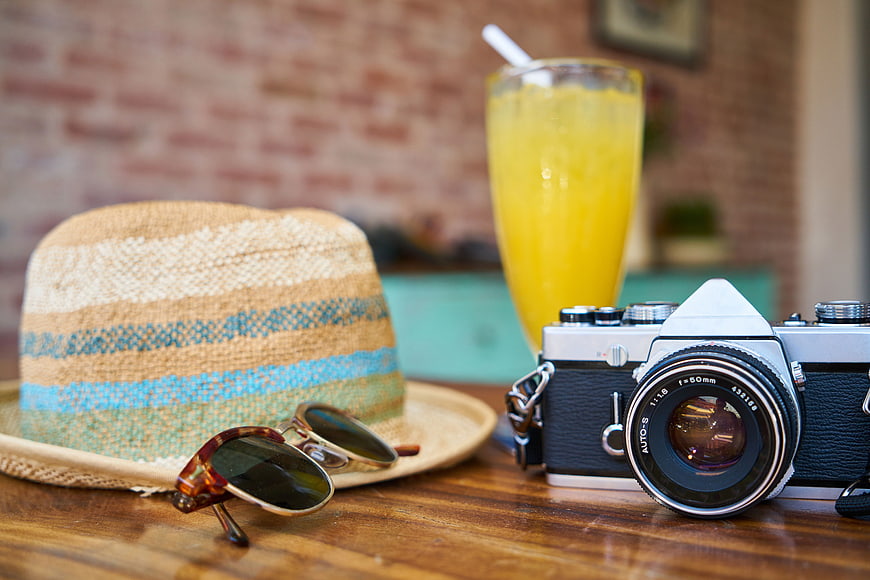 Vintage Camera, Straw Hat, and Sunglasses on Wooden Table