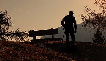 Silhouette of a hiker resting on a wooden bench in the mountains at sunset