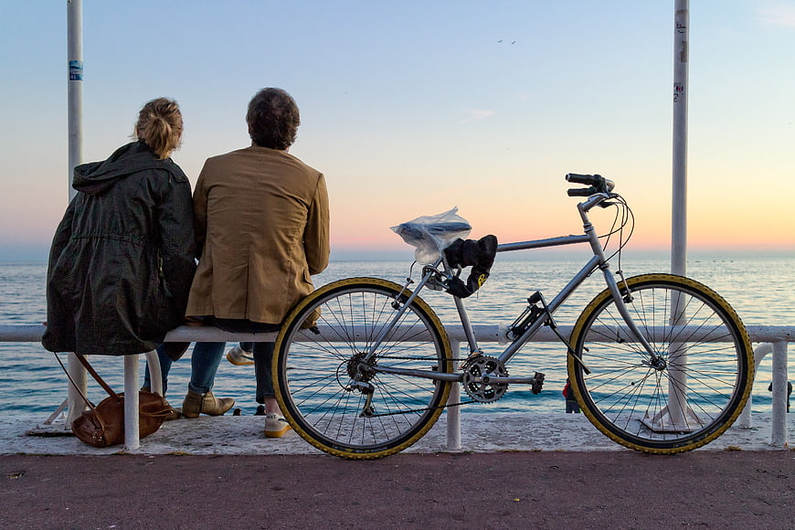 Couple sitting on bench by sea with bicycle at sunset