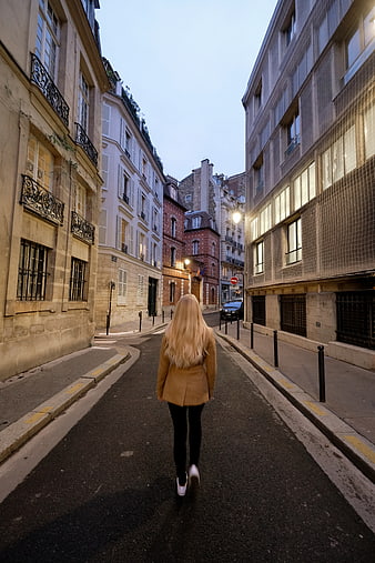 Blonde Woman Walking Down Narrow European Street at Dusk