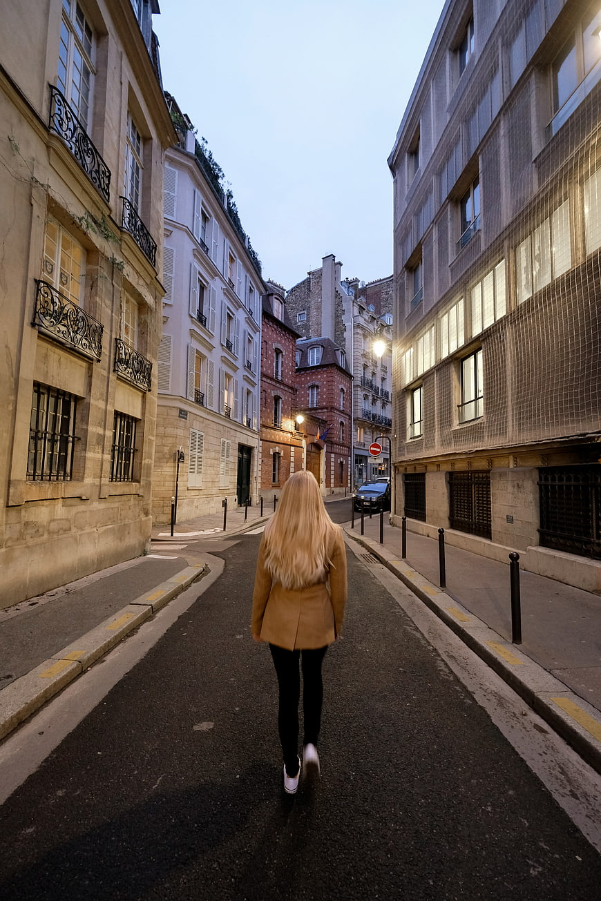Blonde Woman Walking Down Narrow European Street at Dusk