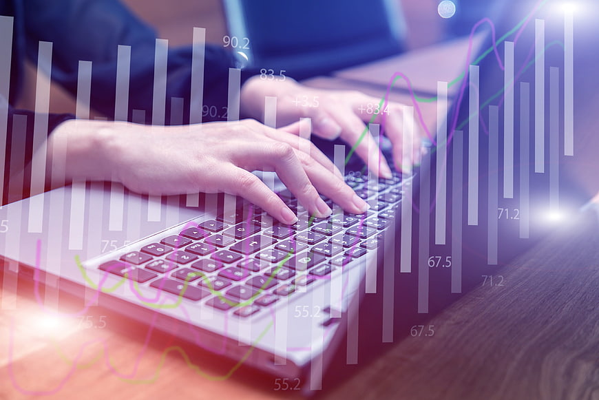 Hands typing on laptop with financial data overlay
