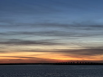 Silhouette of bridge over water at sunset with orange and blue sky