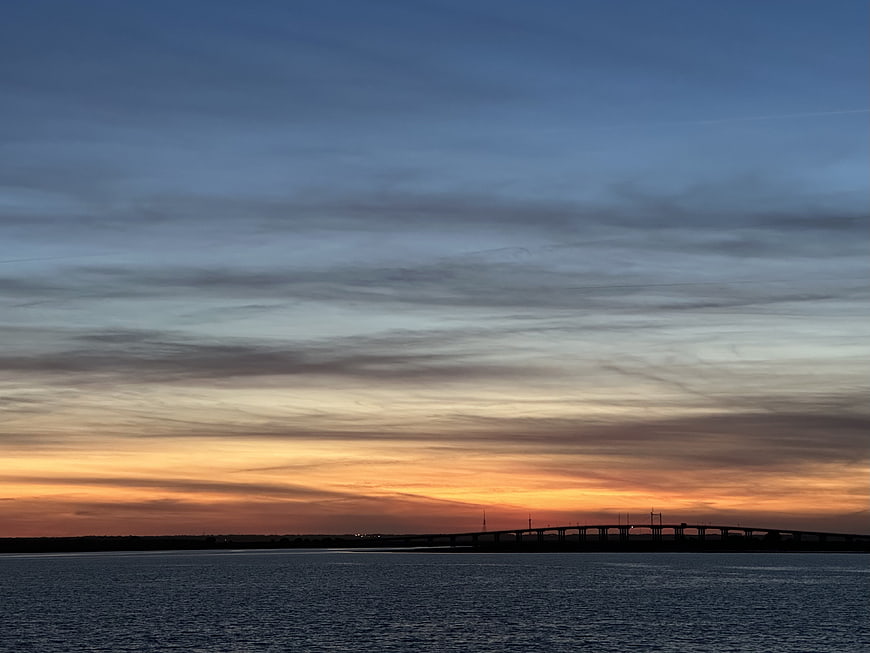 Silhouette of bridge over water at sunset with orange and blue sky