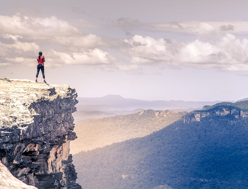 Woman standing on cliff edge overlooking vast mountain landscape