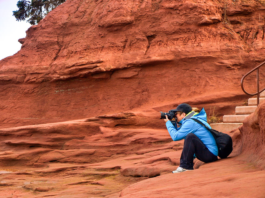 Woman Photographer Crouching with Camera on Red Rock Cliff