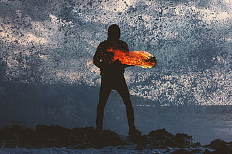 Silhouette of person breathing fire on rocky beach at night