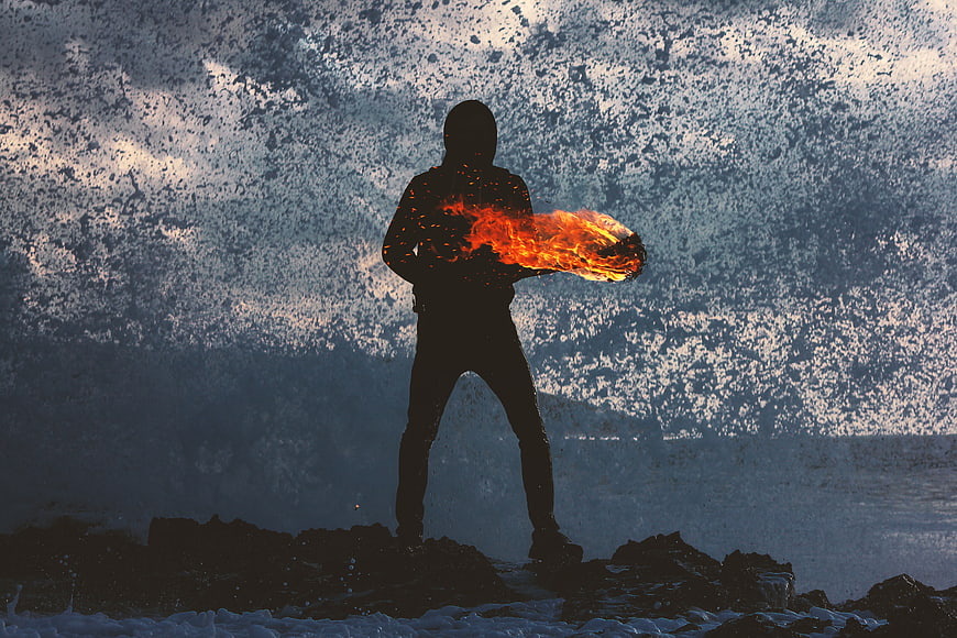 Silhouette of person breathing fire on rocky beach at night
