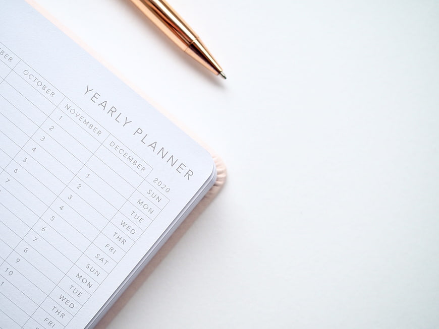 Minimalist Yearly Planner Notebook With Rose Gold Pen On White Surface