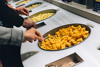 Hands selecting cubed yellow cheese at a tasting counter