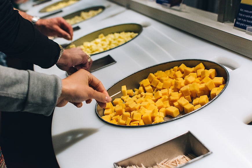 Hands selecting cubed yellow cheese at a tasting counter