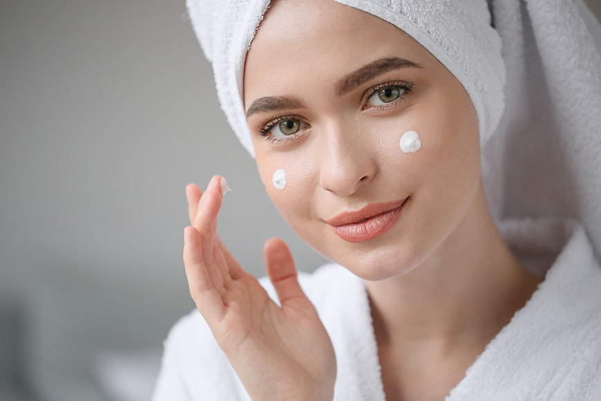 Woman applying face cream with towel on head