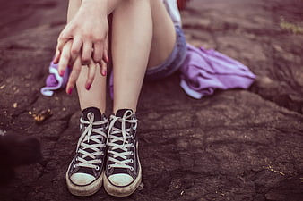 Young woman sitting on rock wearing black sneakers