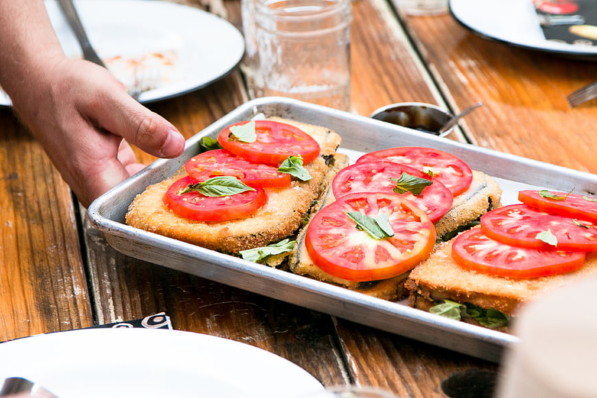 Hand serving tray of fried sandwiches with fresh tomatoes