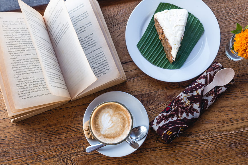 Top view of coffee, cake, and open book on wooden table