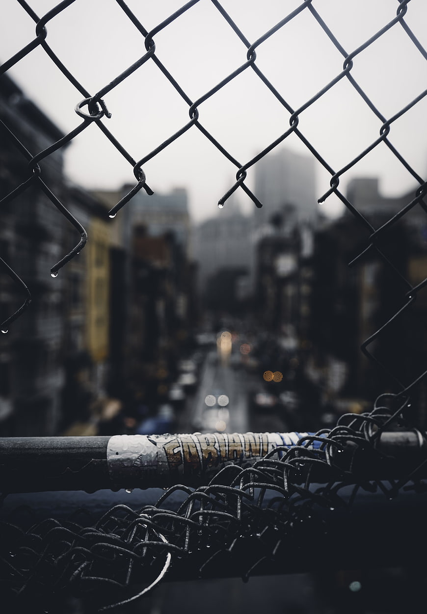 Rainy urban street view through chain link fence