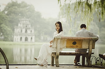 Woman in White Dress Sitting on Park Bench by Lake