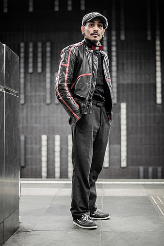 Stylish man in leather jacket and flat cap standing outdoors