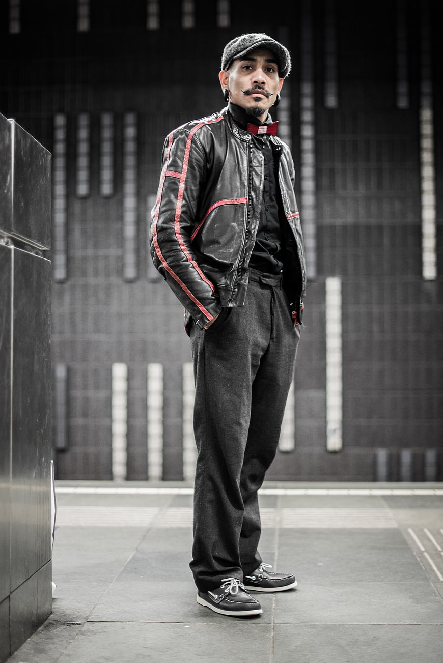 Stylish man in leather jacket and flat cap standing outdoors