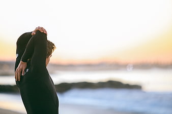 Man in Wetsuit Stretching on Beach at Sunset