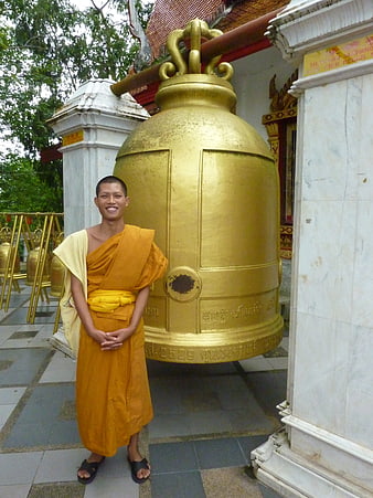 Smiling Buddhist Monk Standing by Large Golden Temple Bell