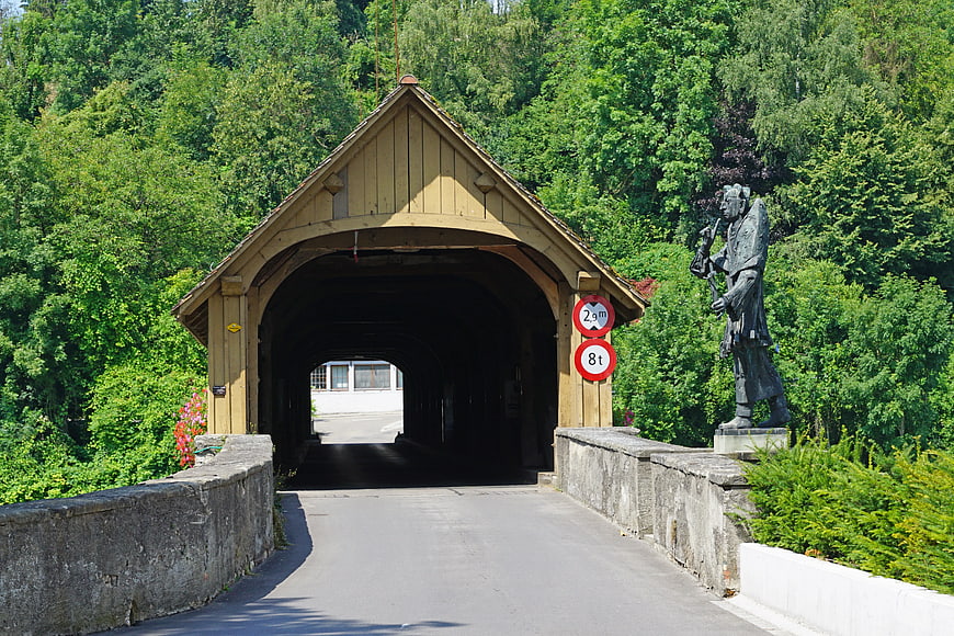 Covered wooden bridge with statue in lush green forest