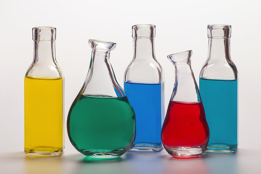 Five glass bottles containing yellow, green, blue, red, and cyan liquids