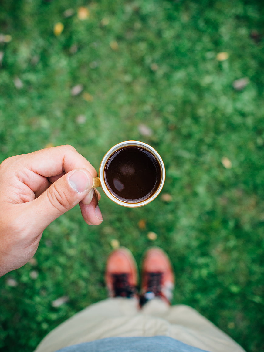 First-person view holding coffee cup over green grass