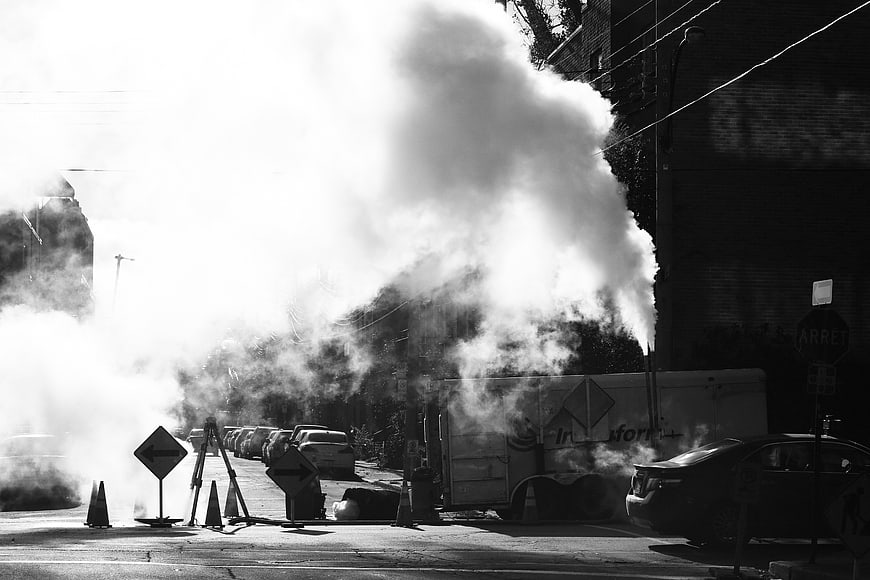 Black and white street scene with steam rising from manhole