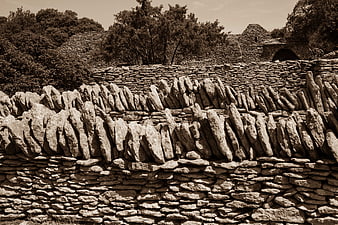 Sepia-toned dry stone wall with vertical capstones and rural architecture