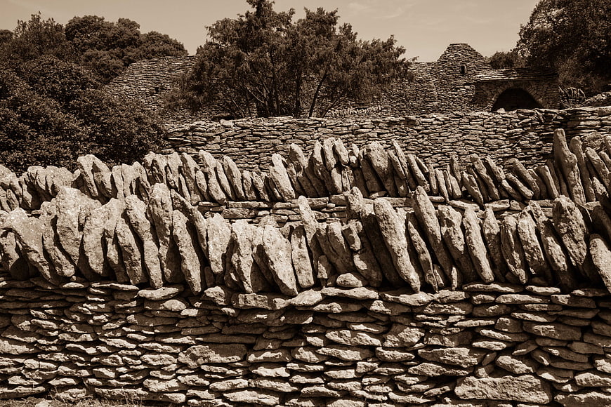 Sepia-toned dry stone wall with vertical capstones and rural architecture