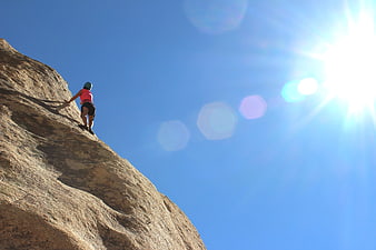 Rock Climber Scaling Cliff Face Against Blue Sky