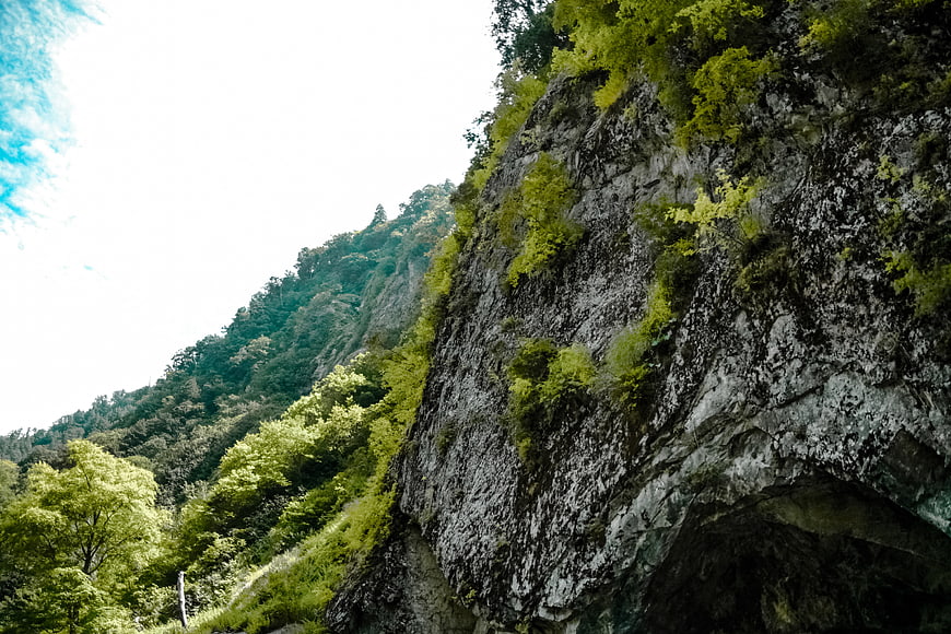 Steep Rocky Cliff Face with Lush Green Vegetation and Blue Sky