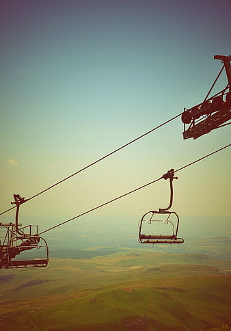 Empty chairlift seats over rolling green hills and blue sky