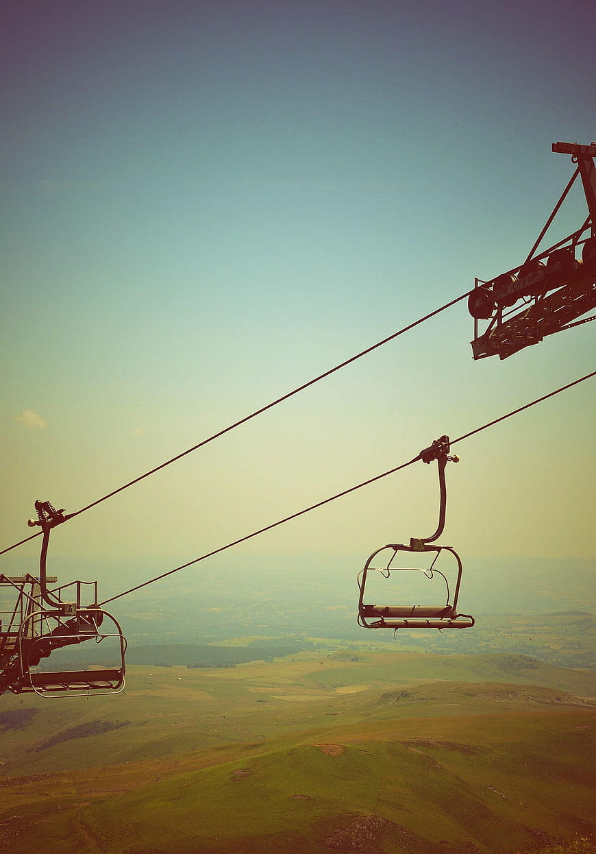 Empty chairlift seats over rolling green hills and blue sky