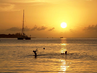 Silhouettes of children playing in ocean at golden sunset