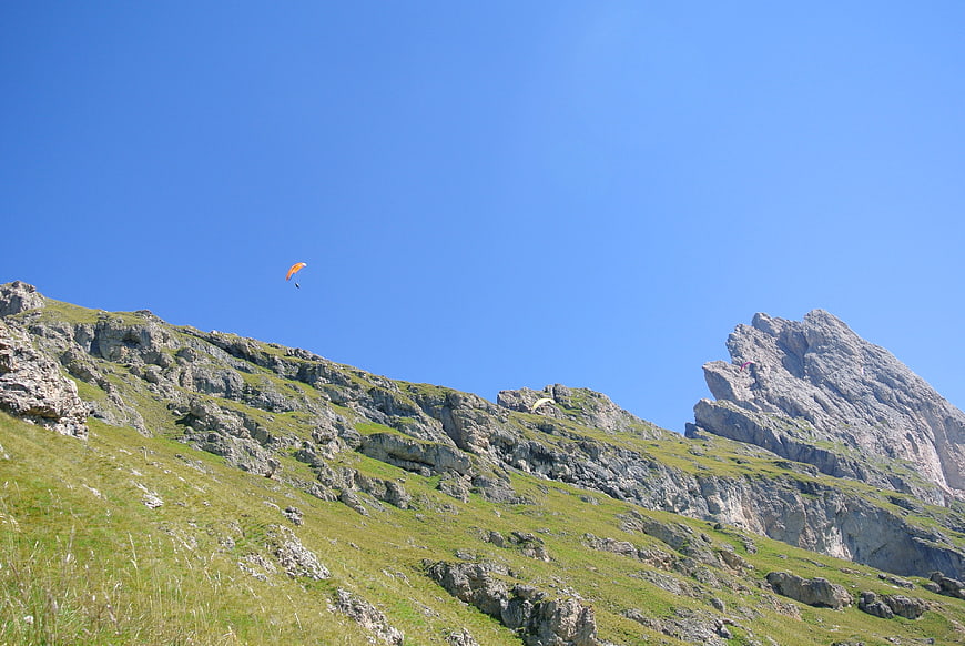 Paraglider soaring over green alpine mountains under blue sky
