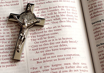 Silver crucifix resting on open Bible page with Lord's Prayer text