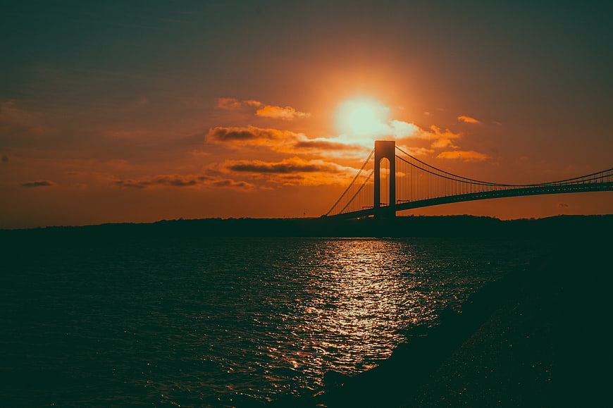 Silhouette of suspension bridge over water at sunset