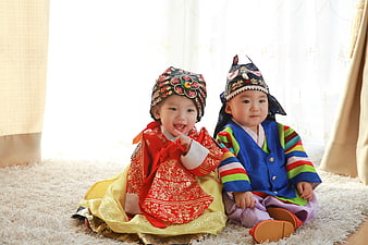 Two babies wearing traditional Korean hanbok sitting on a white rug