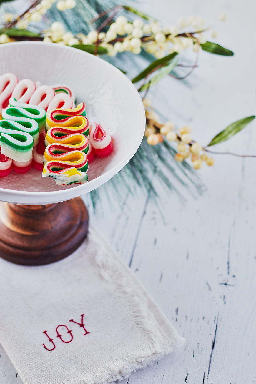 Colorful Christmas ribbon candies on white pedestal with JOY napkin