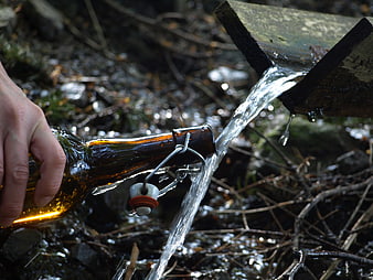Hand filling glass bottle with fresh water from wooden spout