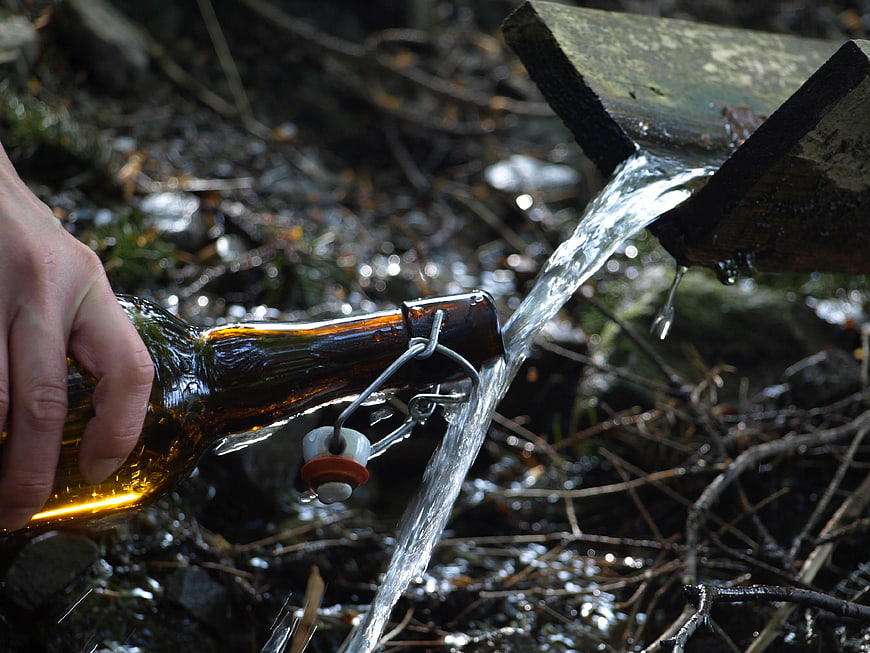 Hand filling glass bottle with fresh water from wooden spout