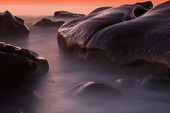 Misty coastal rocks at sunset with smooth water