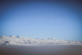 Snowy mountain range above clouds with airplane contrail