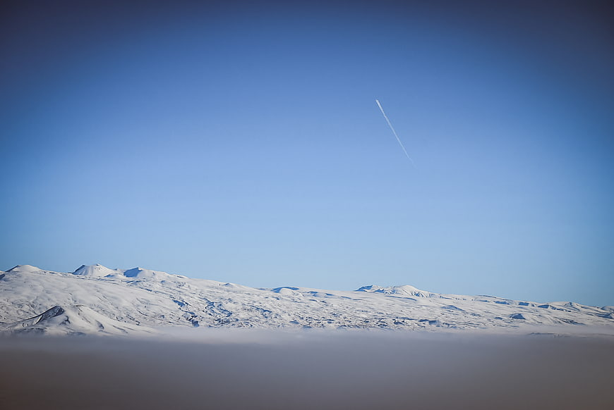 Snowy mountain range above clouds with airplane contrail